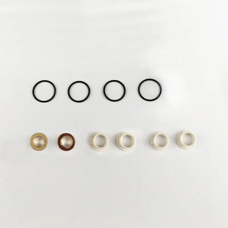 Fünf schwarze O-Ringe und sechs weiße Kunststoffringe, mit zwei Metallringen auf einer weißen Fläche, Ersatzteile für Vapefly Kriemhild RMC.